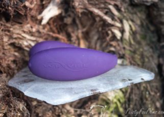 A purple We-Vibe 4+ sits on a perfectly flat piece of ice that is logged partway up a tree. The external prong of the vibrator is facing the camera, so the raised "We-Vibe" logo and the on/off button in the smooth matte silicone is visible.