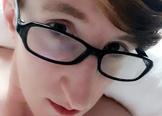 Taylor shown from the shoulders up naked in a bed. The lighting is very soft