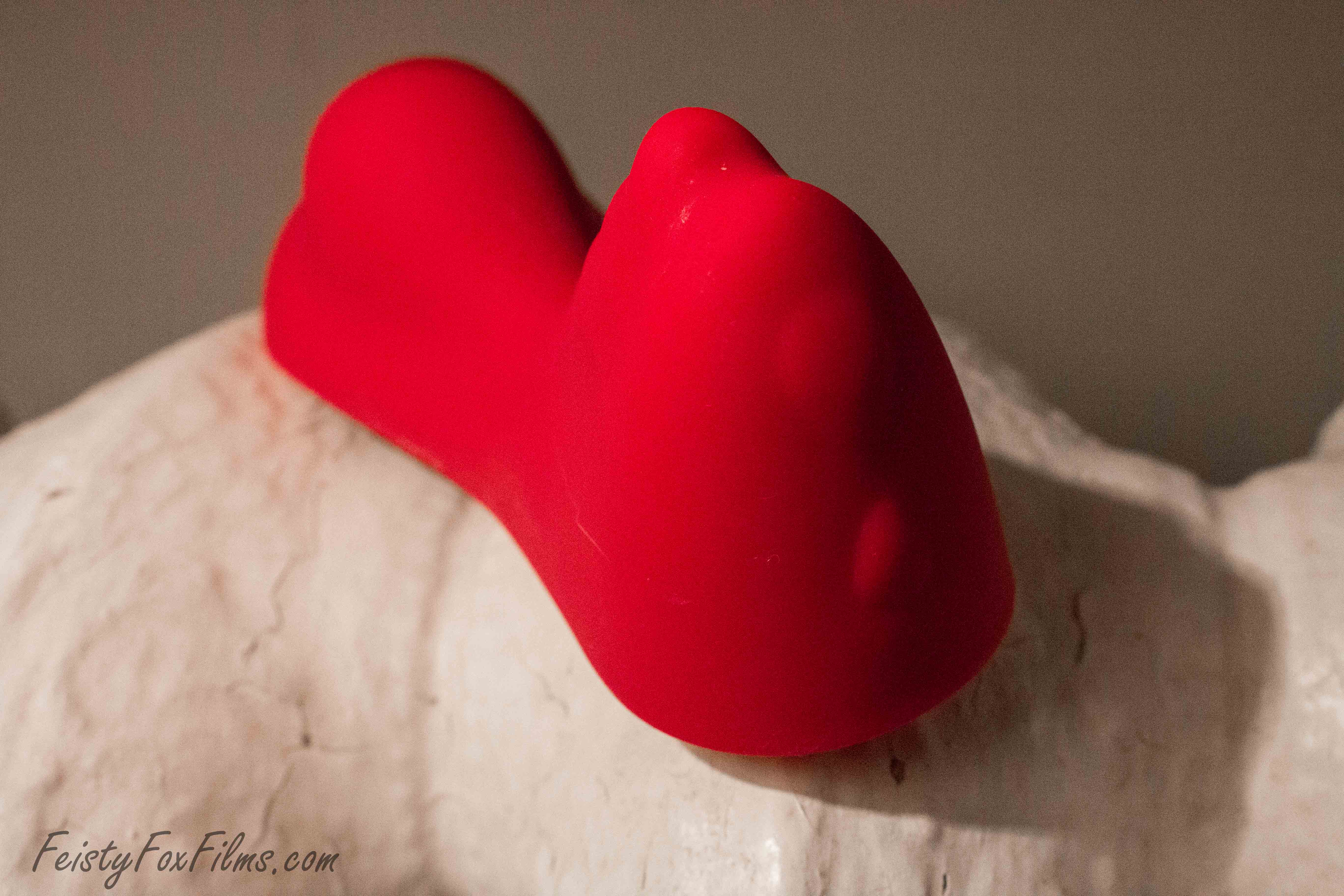 The Ruby Glow sits on top of an old, ornate white radiator. It is angled so you can see the two control buttons and the top of the ridges on the clitoral stimulator. The mound that stimulates the vaginal opening and the perineum can be seen in the background