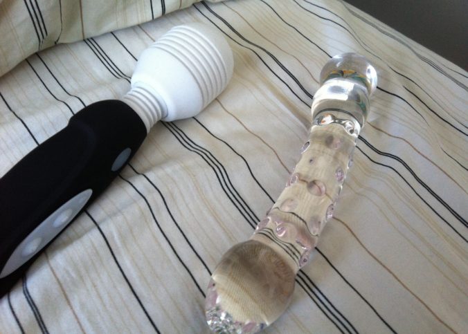 the mystic wand and a glass dildo lie side by side on a bed